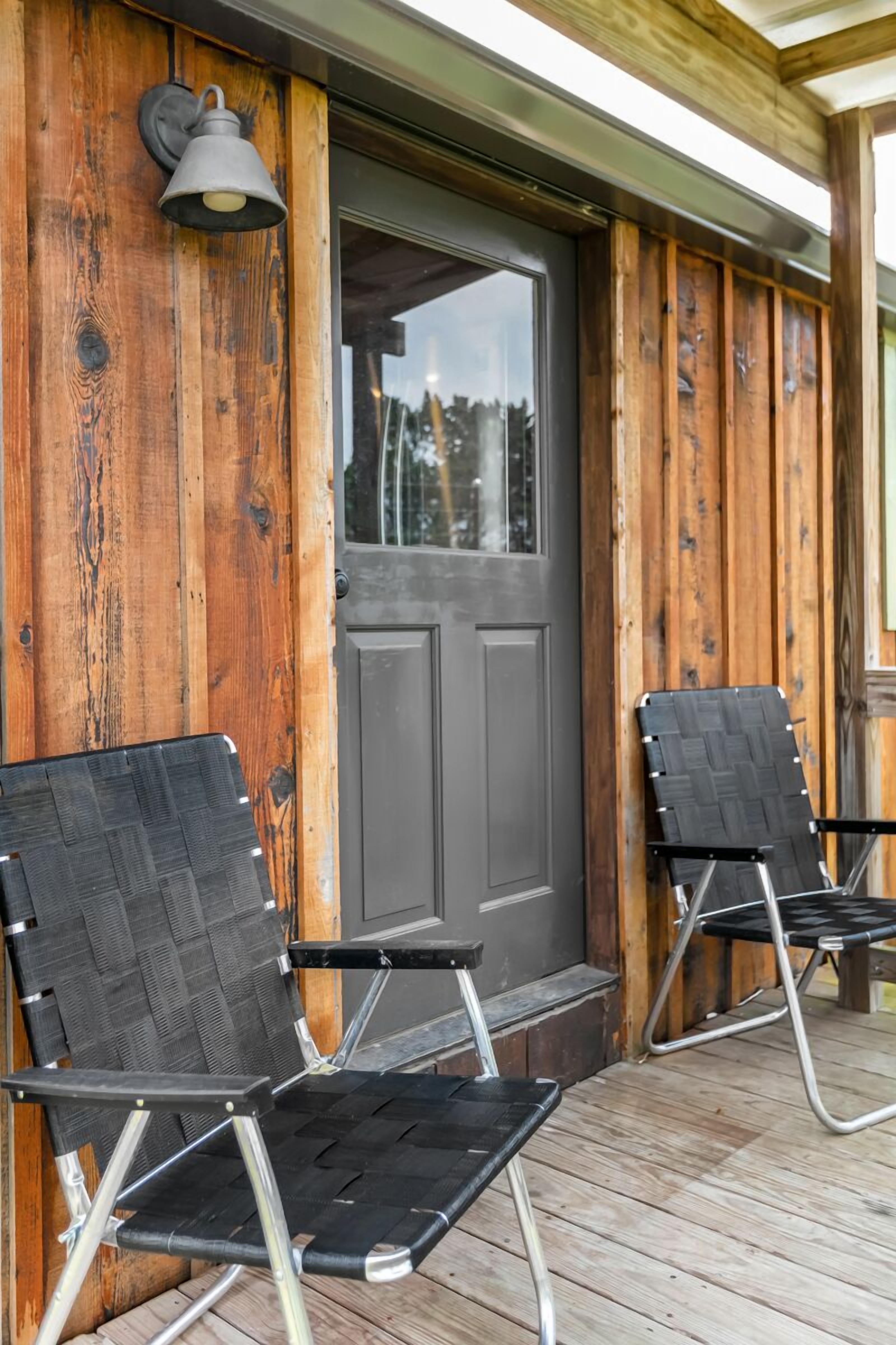 A wooden porch with two black chairs and a door.
