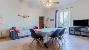 A living room with a sofa, dining table, chairs, a ceiling fan, a TV, and a window.