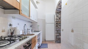A compact kitchen with a gas stove, white cabinets, and a stone wall.