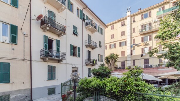 A multi-story residential building with balconies, a gated entrance, and a small garden area.