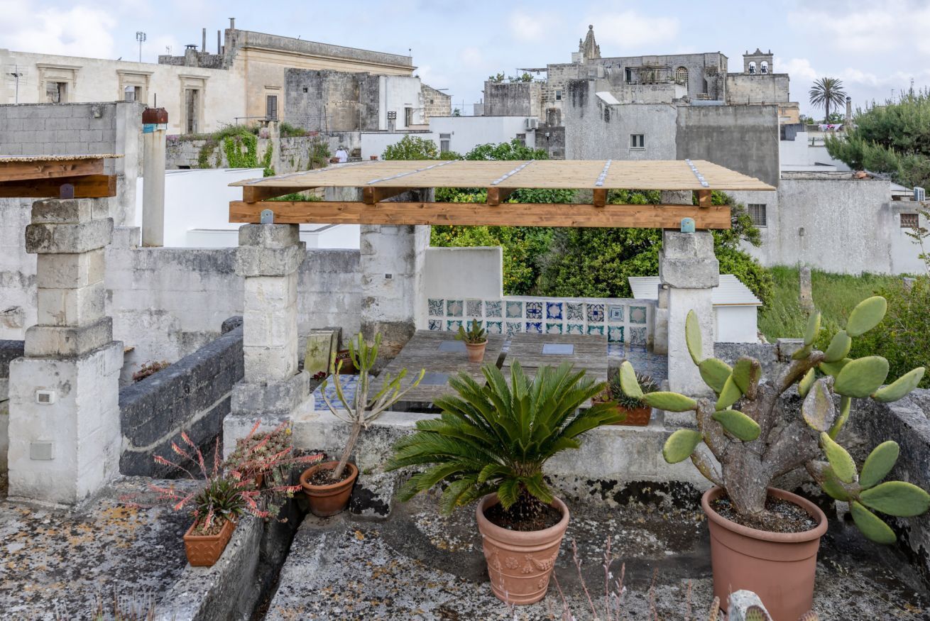 A rooftop garden with potted plants, a wooden pergola, and a view of surrounding buildings.