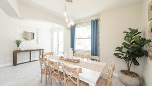 Zona pranzo con tavolo bianco, sedie di legno e lampadario.