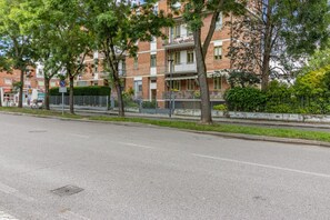 A multi-story residential building with balconies, a paved street, and a metal fence.