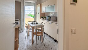 Een compacte keuken met een eethoek, een televisie boven de aanrecht en een schuifdeur naar een buitenbalkon.