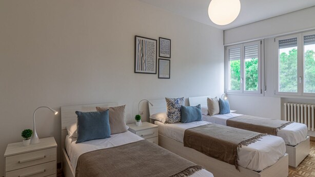 Een slaapkamer met twee bedden, een nachtkastje met een lamp, een kleine plant en kunstwerken in een lijst aan de muur.