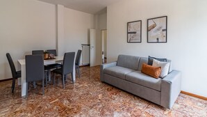 Een moderne woonkamer met een grijze bank, een eettafel met stoelen en twee abstracte schilderijen aan de muur.