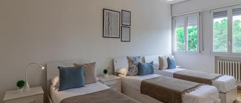 Ein Schlafzimmer mit zwei Betten, einem Nachttisch mit Lampe, einer kleinen Pflanze und gerahmten Bildern an der Wand.
