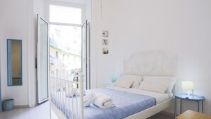 A bedroom with a bed, a bedside table, a nightstand, a window, and a door.