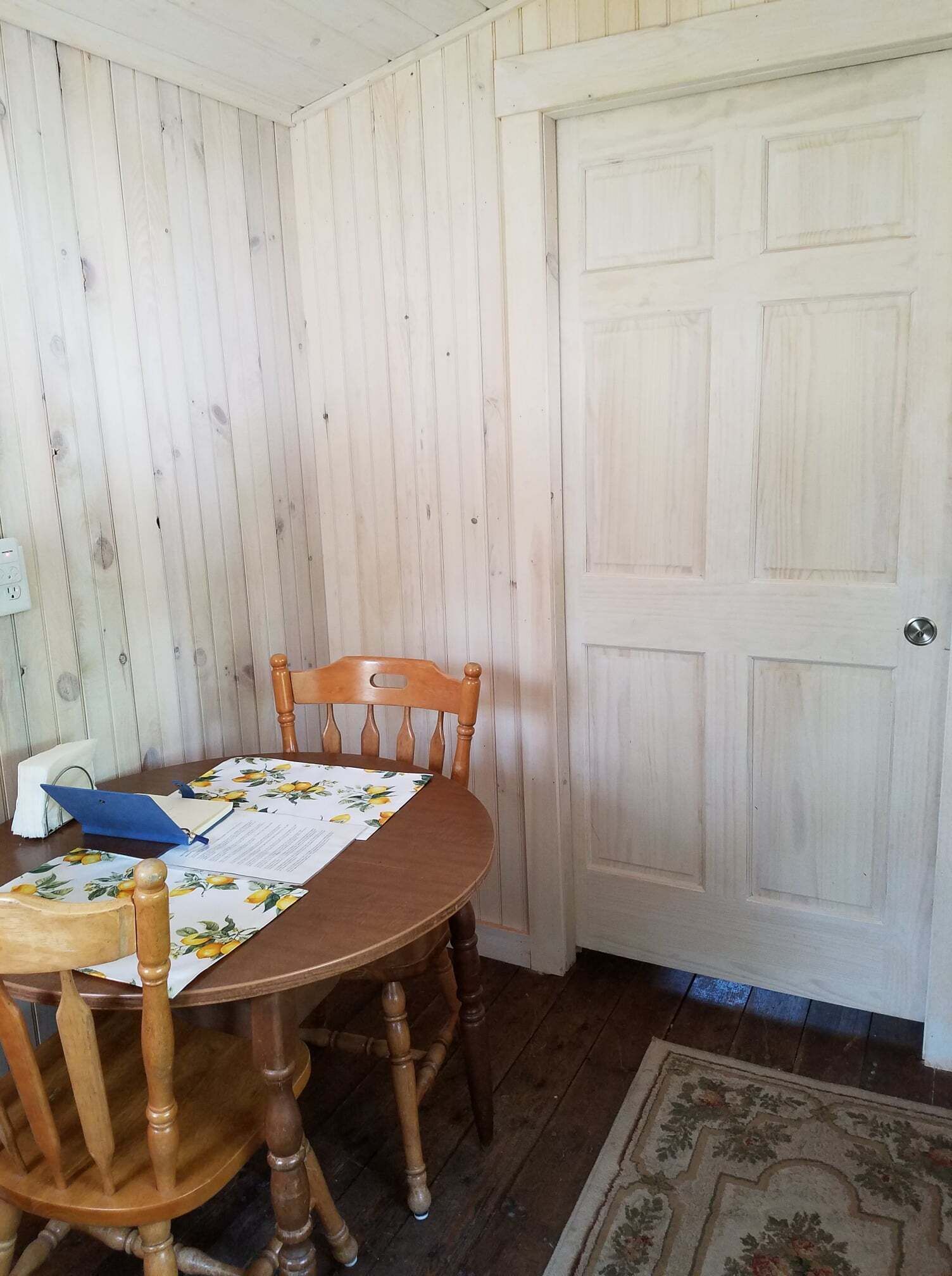 Un coin repas avec une table et des chaises en bois, une porte blanche et un tapis à motifs.