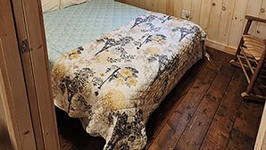 Una habitación de madera con una cama, un ventanal con cortinas a cuadros y una lámpara en el techo.