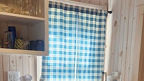 Una cocina compacta con armarios de madera, una ventana con cortina a cuadros y varios electrodomésticos.