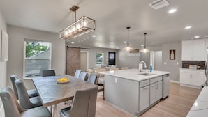 Une cuisine moderne dotée d’un îlot central, d’un coin repas avec une table et des chaises, et d’un espace de vie comprenant un canapé et une table basse.