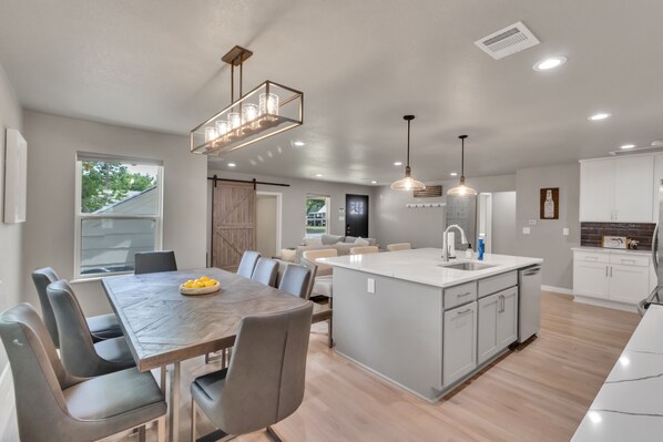 A modern kitchen with a central island, dining area with a table and chairs, and a living space with a sofa and coffee table.