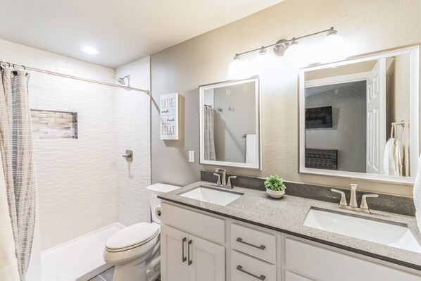 Un baño moderno con dos lavamanos, un inodoro, una ducha y un espejo.