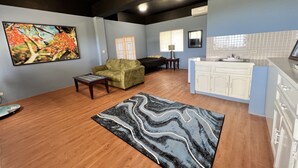 A living room with a sofa, a coffee table, a rug, a painting, and a kitchen area with cabinets and a sink. - Ocean View Capitol Hill Studio with Sunset Deck (Capitol Hill)