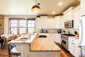 A kitchen with white cabinets, a granite countertop, a built-in oven, a microwave, and a large window.