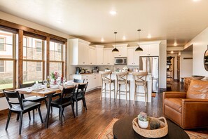 A spacious kitchen with white cabinets, a dining area with a wooden table and chairs, and a leather sofa.