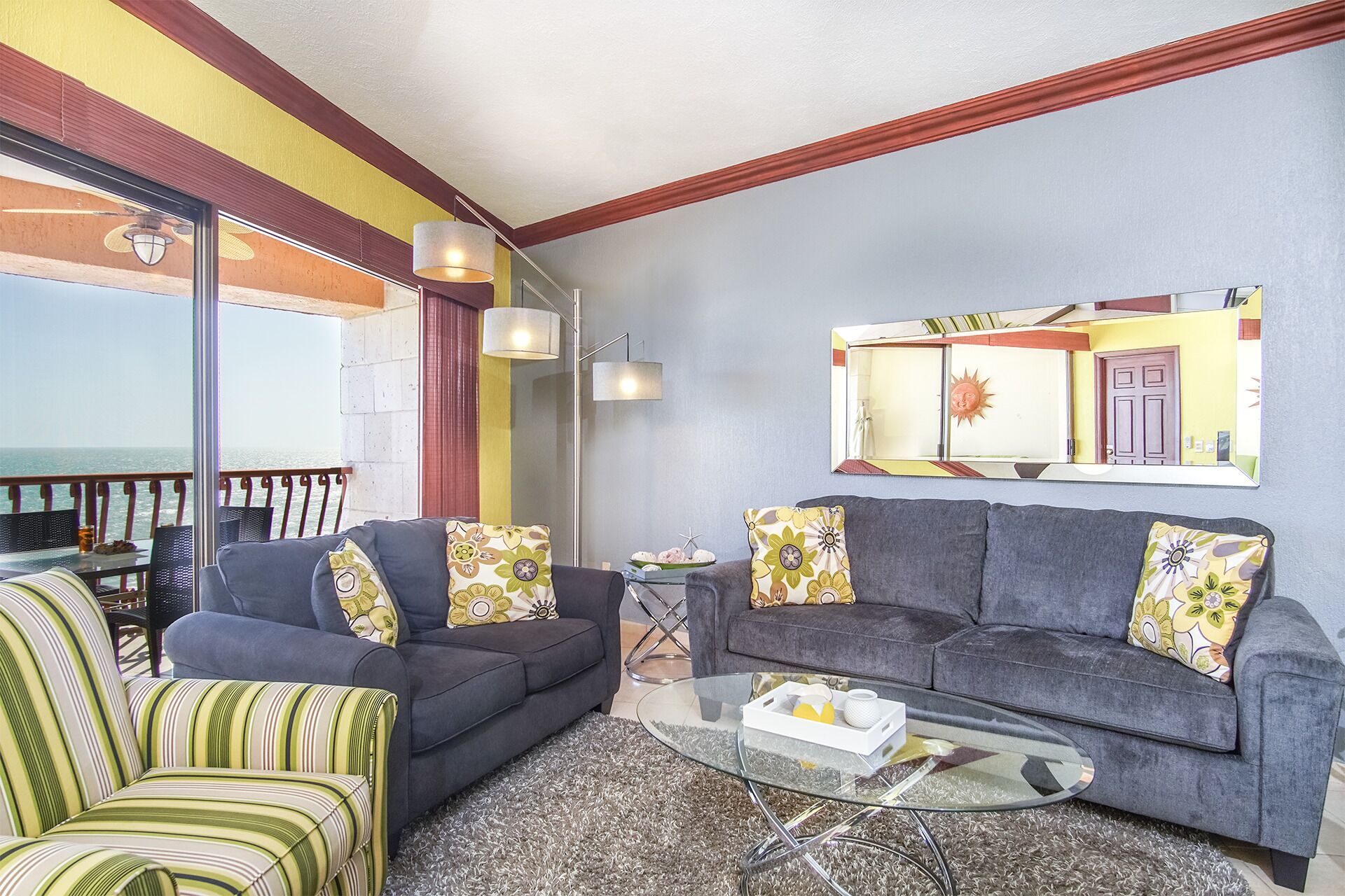 A living room with a sofa, armchairs, a glass coffee table, and a view of the sea through large windows.