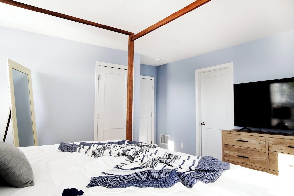 Een slaapkamer met een hemelbed, een televisie op een houten kast en twee witte deuren.