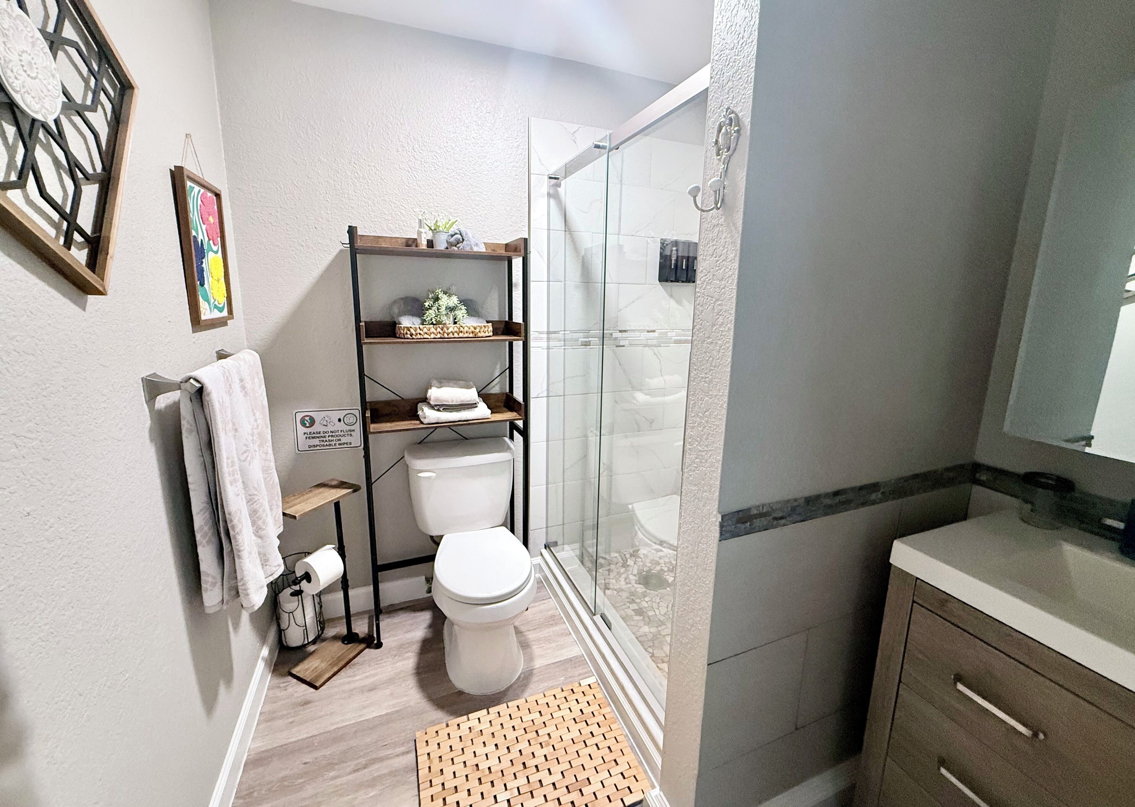 A bathroom with a toilet, shower, and shelves with toiletries.