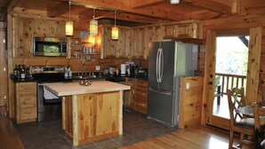 A wooden cabin with a kitchen featuring a central island, a refrigerator, and a dining area with a chair. - Amazing Views! Hot Tub!! Minutes from the Gorge!!! (Stanton)
