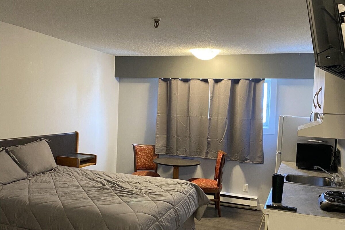 A bedroom with a bed, a chair, a desk with a computer, and a television.