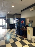 Piso xadrez, máquinas de venda automática, bebedouro e parede com cardápio.