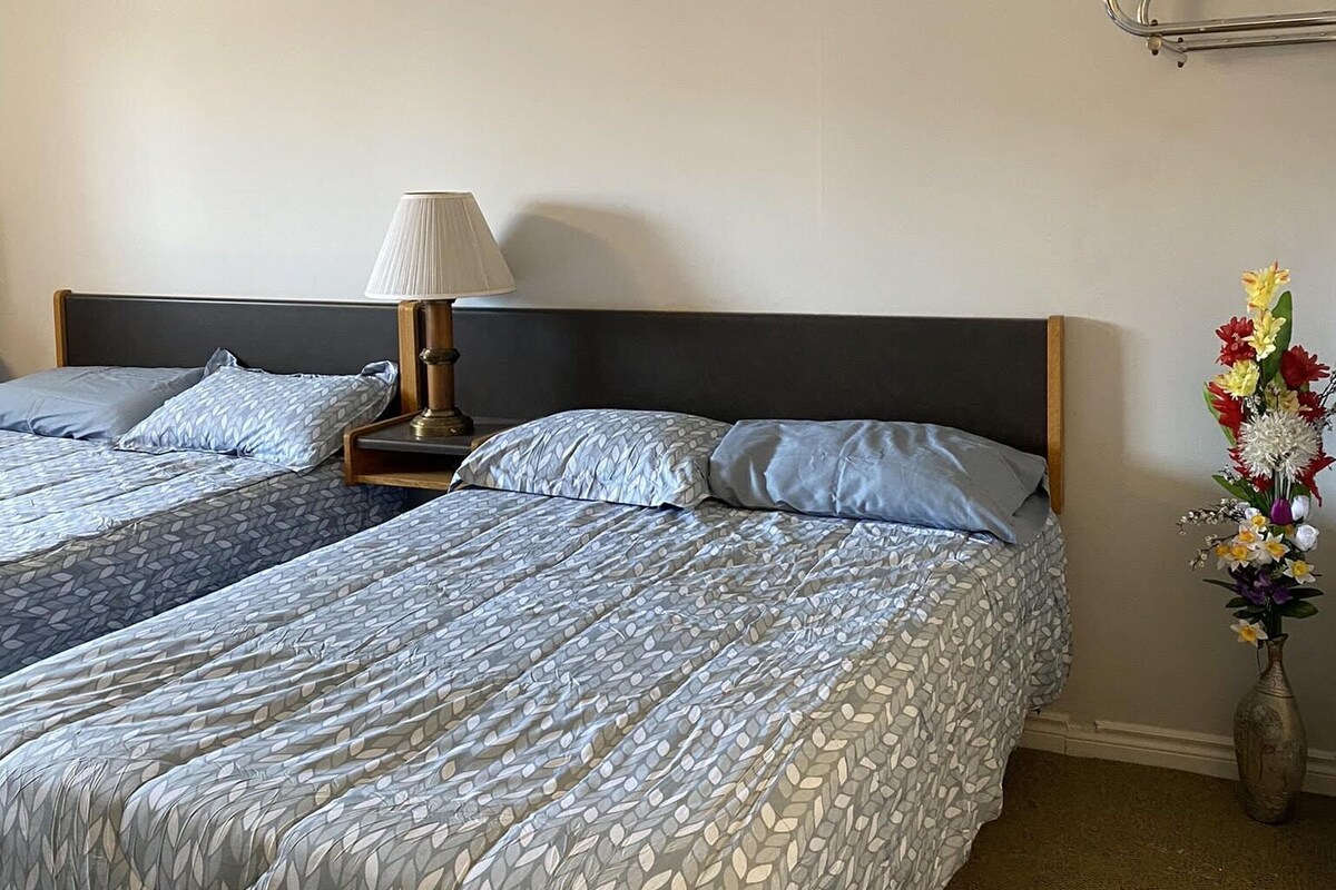 A hotel room with a double bed, a bedside lamp, a flower vase, and a headboard.