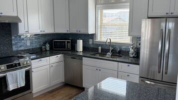 A modern kitchen with white cabinets, a stainless steel refrigerator, a built-in oven, and a granite countertop.