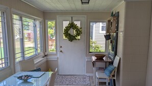 A dining area with a glass table, white chairs, a patterned rug, and a door with a wreath. - Cozy Pet Friendly Cottage, Partial Water View, Sleeps 7, Half Block from Beach! (Lexington)