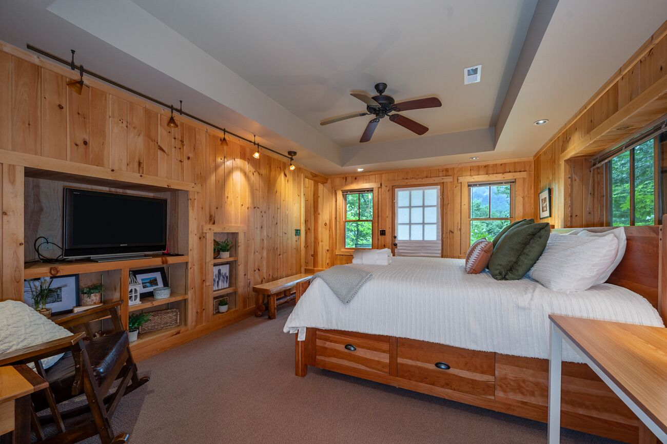 Un dormitorio de cabaña de madera con cama, televisor, estantes y ventanas.