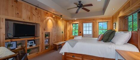 Un dormitorio de cabaña de madera con cama, televisor, estantes y ventanas.