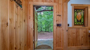 A wooden door leading to a forested area, a patterned rug, and a stained glass window with leaf designs.