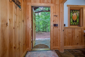 A wooden door leading to a forested area, a patterned rug, and a stained glass window with leaf designs.