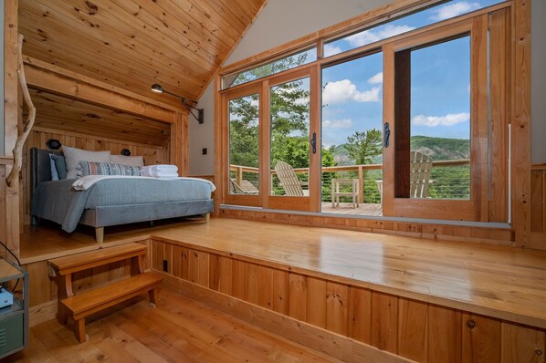 Un dormitorio de cabaña de madera con una cama, un banco y un amplio ventanal que ofrece vistas al exterior.