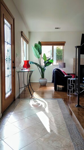 Un salon avec une plante en pot, un vase rouge, une chaise noire et une petite table.