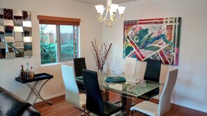A dining area with a glass table, chairs, a chandelier, a window with a view of greenery, and a colorful abstract painting. - Modern Townhouse Suites Chef's Kitchen SoFi FIFA World Cup 2026 Beverly Hills!!! (Los Angeles)