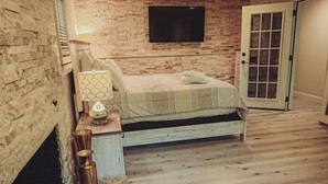 A bedroom with a wooden floor, a bed with striped bedding, a wall-mounted TV, and a door with glass panels. - Beach nearby Pool/HotSpa Firepit LGbackyard (Barnstable)