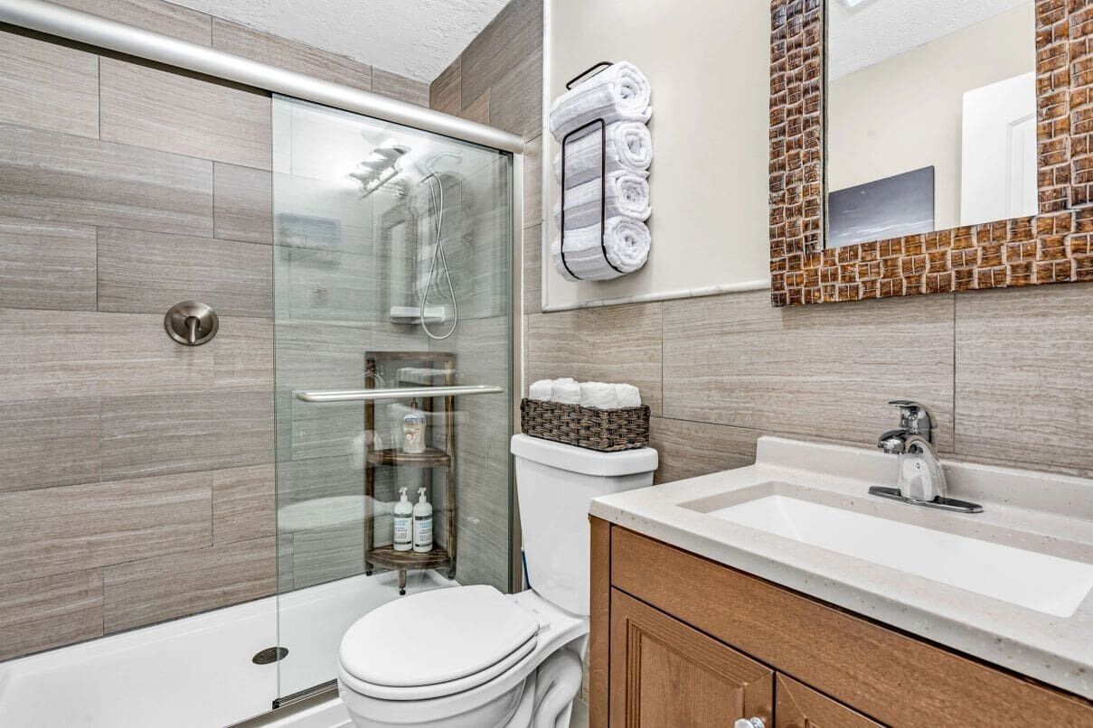 A modern bathroom with a glass shower enclosure, a toilet, a sink with a vanity, and a mirror with a brick-patterned frame.