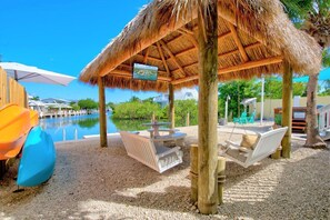 A beachside lounge area with a thatched roof, seating, and a pool view. - Pineapple Sea Shack: 60' Dock, Tiki Hut, Swim Spa, Kayaks, Paddleboards & Pets (Marathon)
