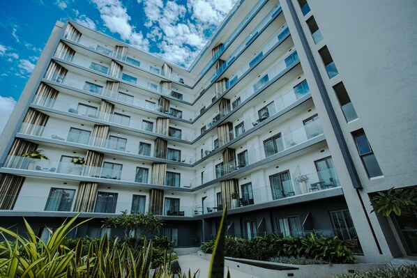 Un edificio de varios pisos con balcones, grandes ventanales y un patio interior con plantas.