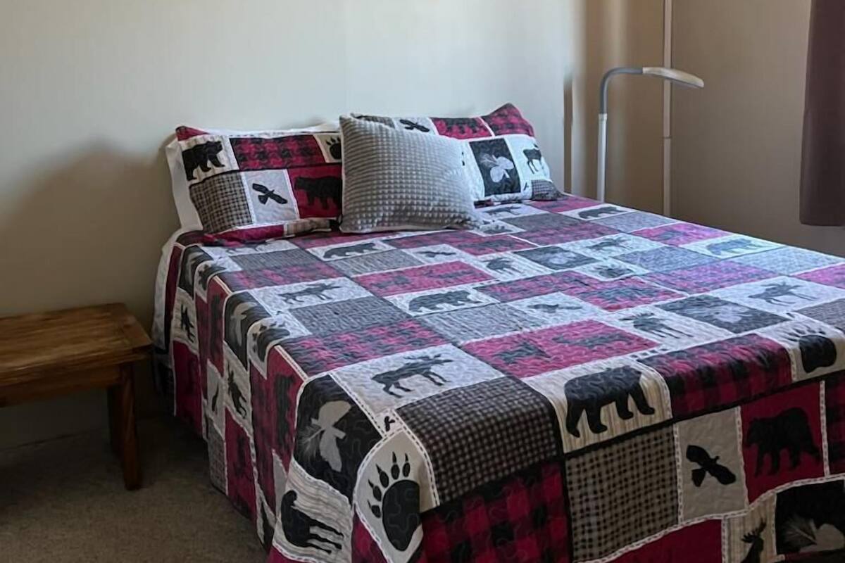 Une chambre à coucher avec un lit recouvert d’une courtepointe patchwork, une table de chevet et une lampe sur pied.