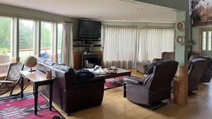 Un salón amplio con un televisor grande, sofás de cuero, una mesa de centro de madera y vistas al exterior a través de amplias ventanas.
