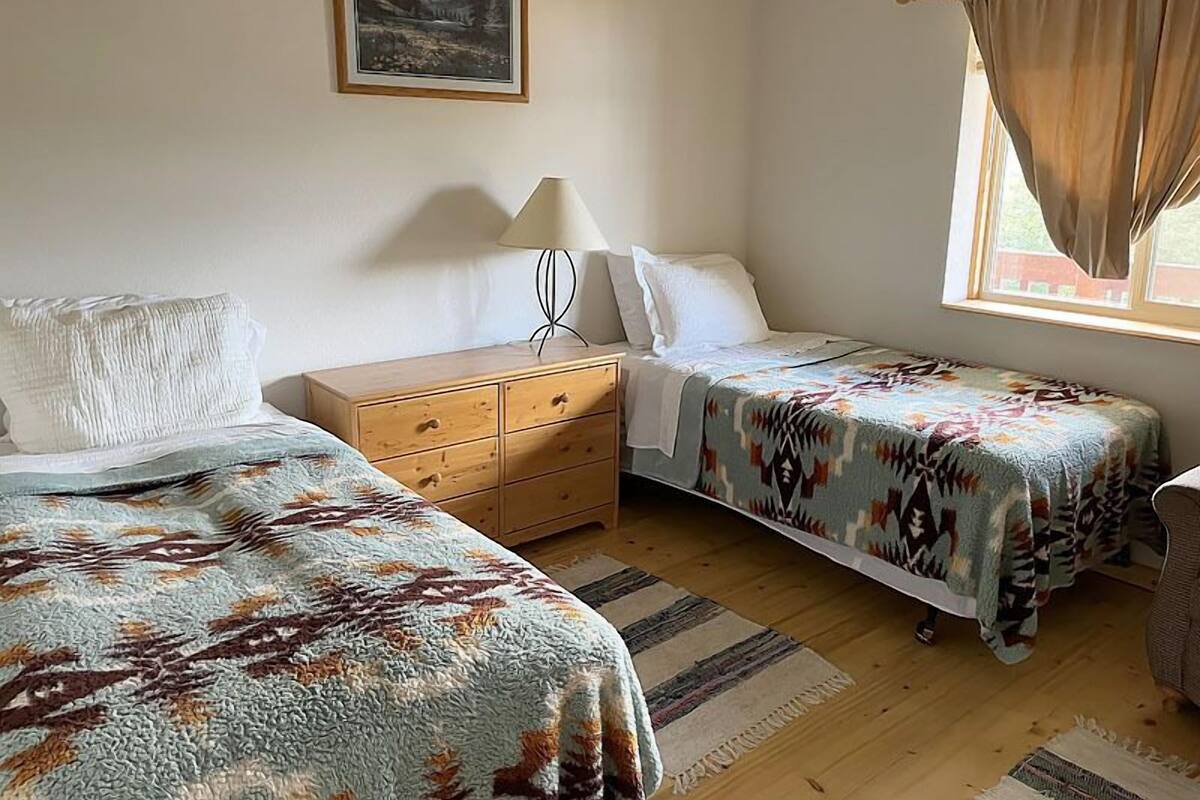 Une chambre avec deux lits, une commode en bois, une lampe et une fenêtre avec des rideaux.