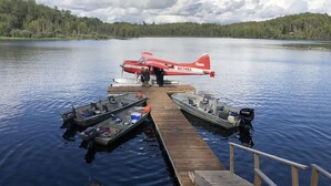 Un pequeño hidroavión rojo en un muelle de madera, con varios barcos amarrados cerca.