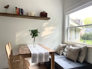 Ein gemütlicher Raum mit einem Holztisch, einer Bank und einem Fenster mit Blick auf ein Haus und Grünflächen.