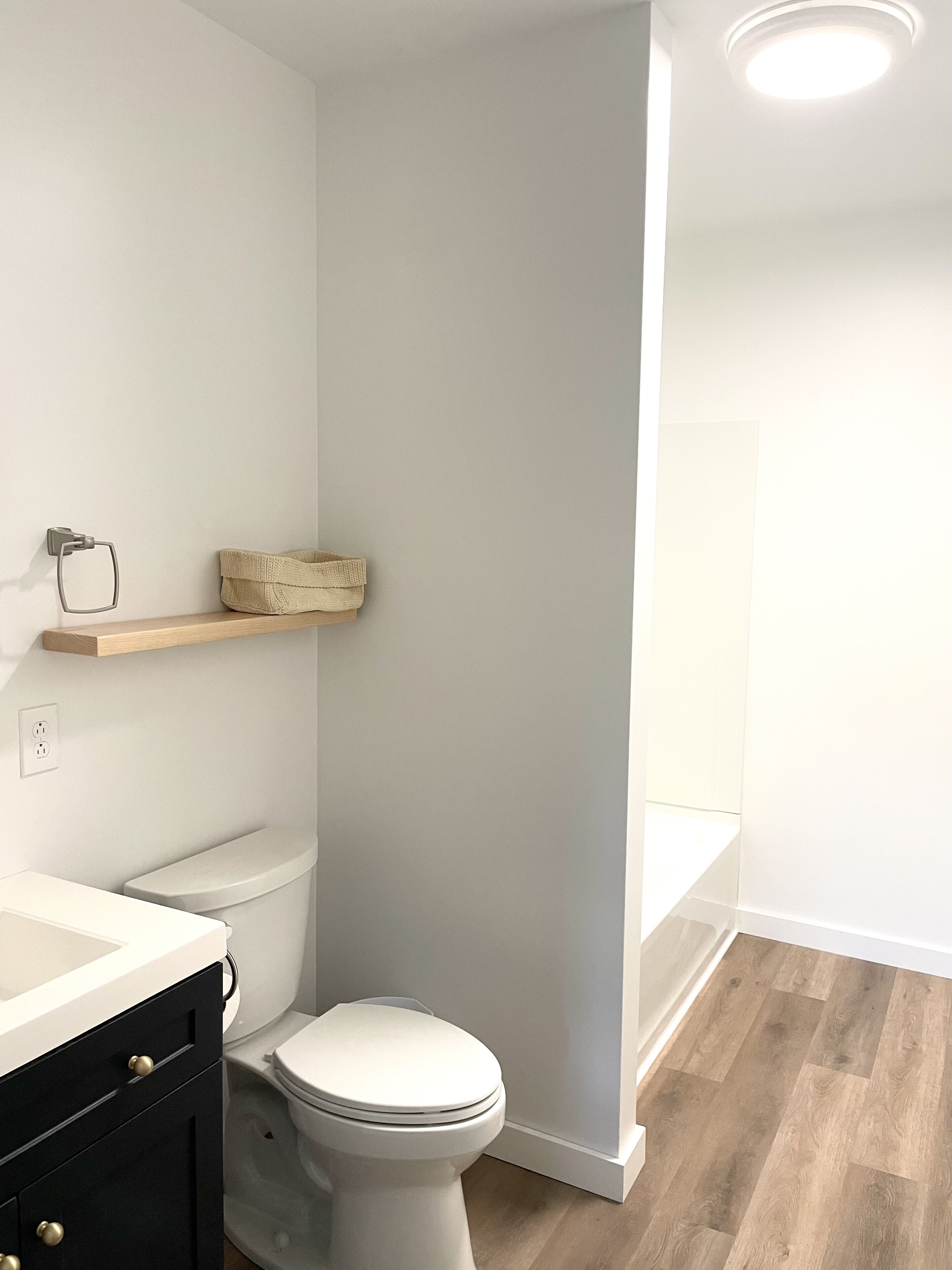 Een badkamer met een wit toilet, een houten plank en een zwart kastje.