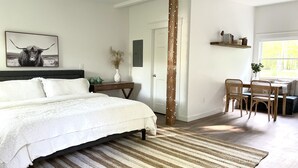 Une chambre à coucher avec un lit, un bureau et des chaises. On y trouve une porte, une fenêtre et une étagère fixée au mur, sur laquelle sont posés divers objets.