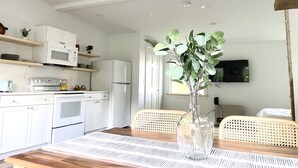 Une cuisine moderne avec des appareils électroménagers blancs, une table à manger agrémentée d’un vase de plantes vertes et des chaises en osier.