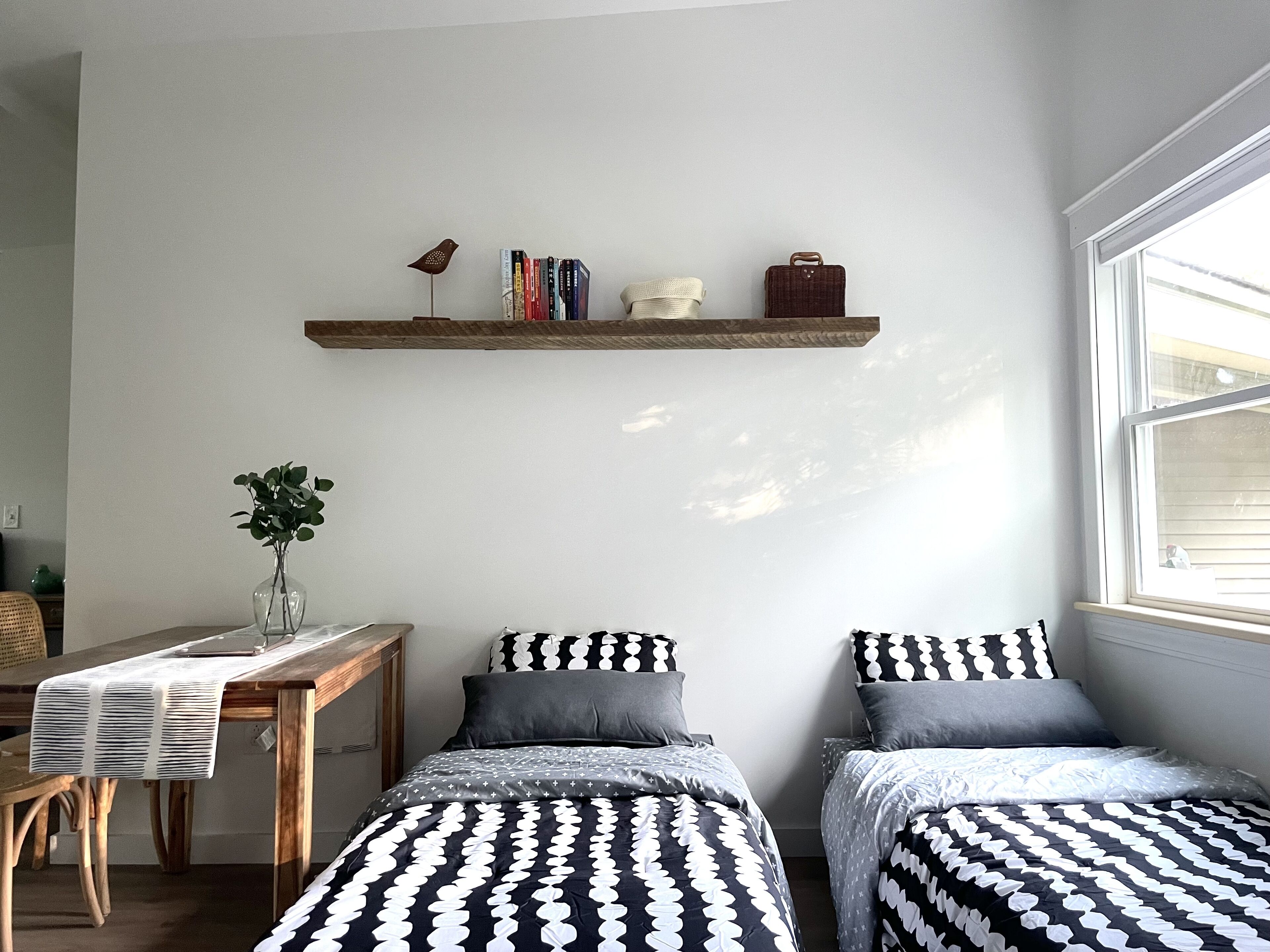Een slaapkamer met twee bedden, een houten bureau, een boekenkast en een raam.